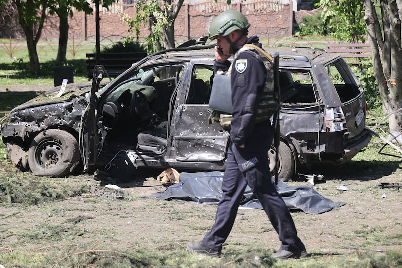 A Ukrainian police officer walks past a body bag near a damaged car in Zolochiv.
