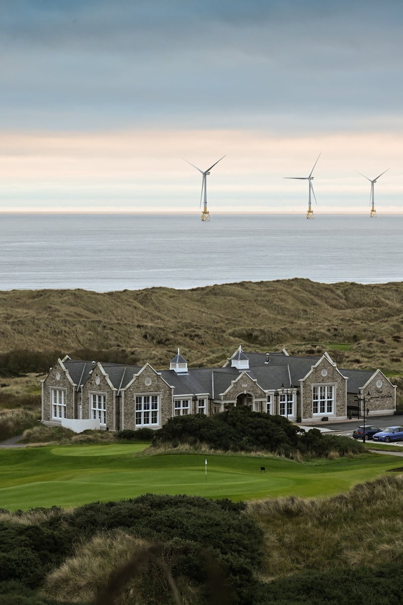 A club house at Trump International Golf Links in Balmedie, Scotland, with water and offshore wind turbines behind it.