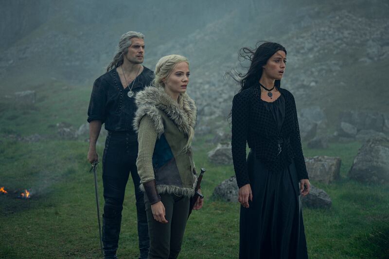 Henry Cavill, Freya Allan, and Anya Chalotra stand in a field from a scene in the third season of The Witcher.