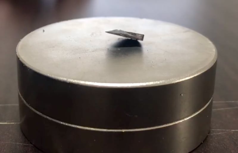 A dark grey material floats above a light grey magnet.