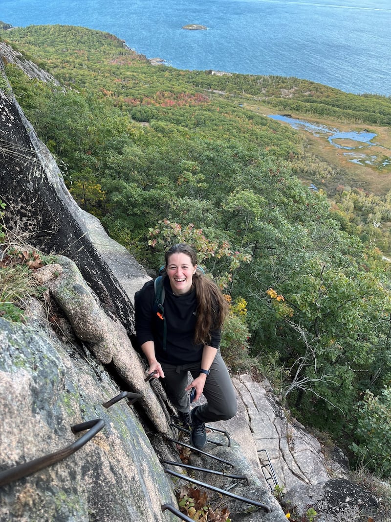 Captain Rebecca Lobach smiling on a cliffside while climbing a via ferrata.