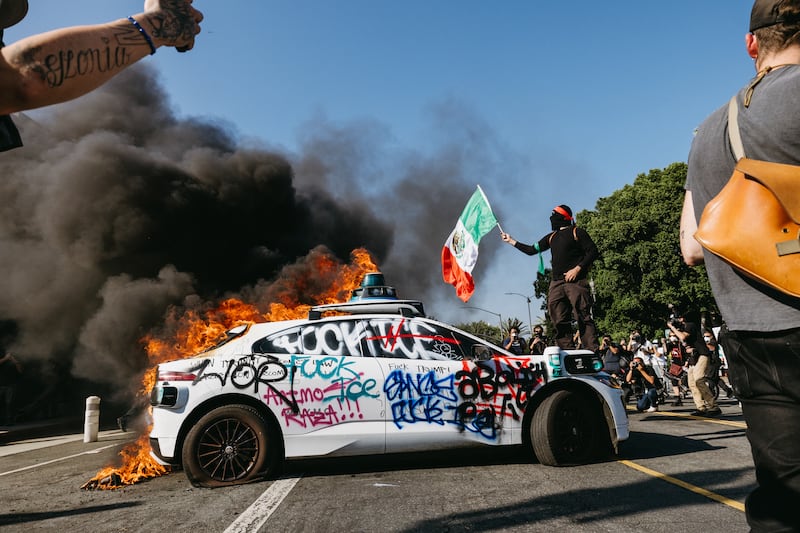 A Waymo vehicle burns in the street as smoke billows during protests in Los Angeles, California, on June 8, 2025.
