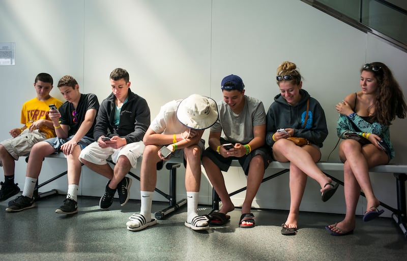 Teens look at their iPhones.