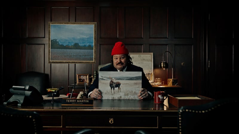 Matty Matheson sits at a desk holding a picture of a moose.