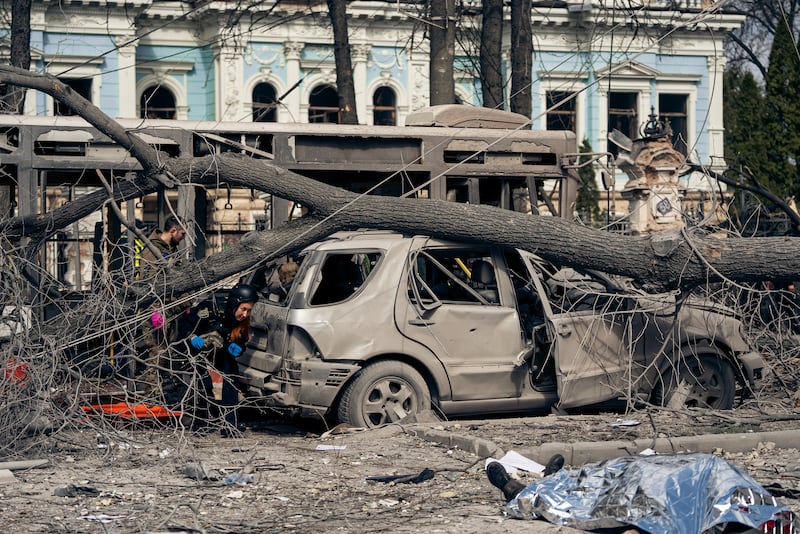 A blown out bus and car and a body covered in a silver blanket after Russia's Palm Sunday attack in the Ukrainian city of Sumy.