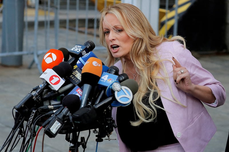Stormy Daniels speaks into a podium filled with reporters’ microphones outside a courthouse.