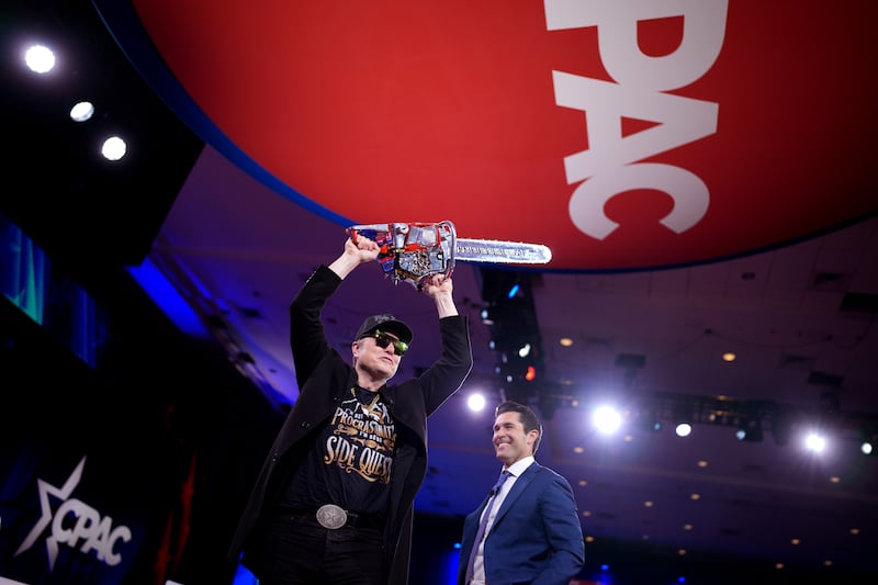 OXON HILL, MARYLAND - FEBRUARY 20: CEO of Tesla and SpaceX Elon Musk wields a chainsaw as he leaves the stage alongside Newsmax anchor Rob Schmitt at the Conservative Political Action Conference (CPAC) at the Gaylord National Resort Hotel And Convention Center on February 20, 2025 in Oxon Hill, Maryland. The annual four-day gathering brings together conservative U.S. lawmakers, international leaders, media personalities and businessmen to discuss and champion conservative ideas. Argentinian President Javier Milei gifted Musk the chainsaw that he used as a prop while campaigning. (Photo by Andrew Harnik/Getty Images)