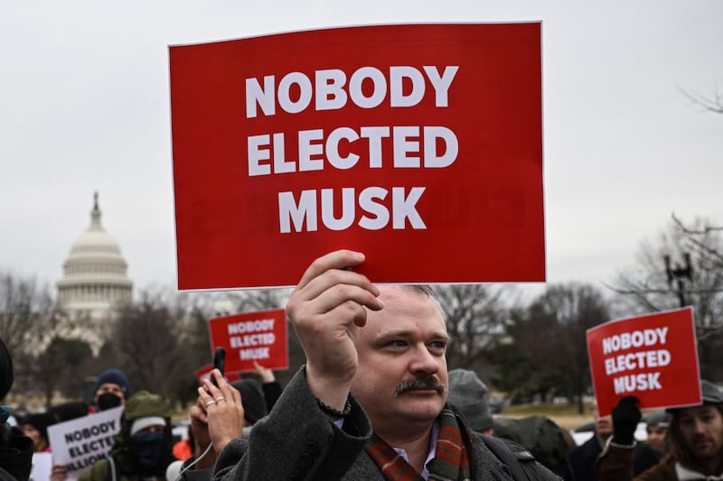 People hold up signs as they protest against US President Donald Trump and Elon Musk's "Department of Government Efficiency" (DOGE) outside of the US Department of Labor near the US Capitol in Washington, DC, February 5, 2025. Elon Musk has begun swinging his wrecking ball at the US government, with concerns growing over the unprecedented power that President Donald Trump has handed to the world's richest man. (Photo by Drew ANGERER / AFP) (Photo by DREW ANGERER/AFP via Getty Images)