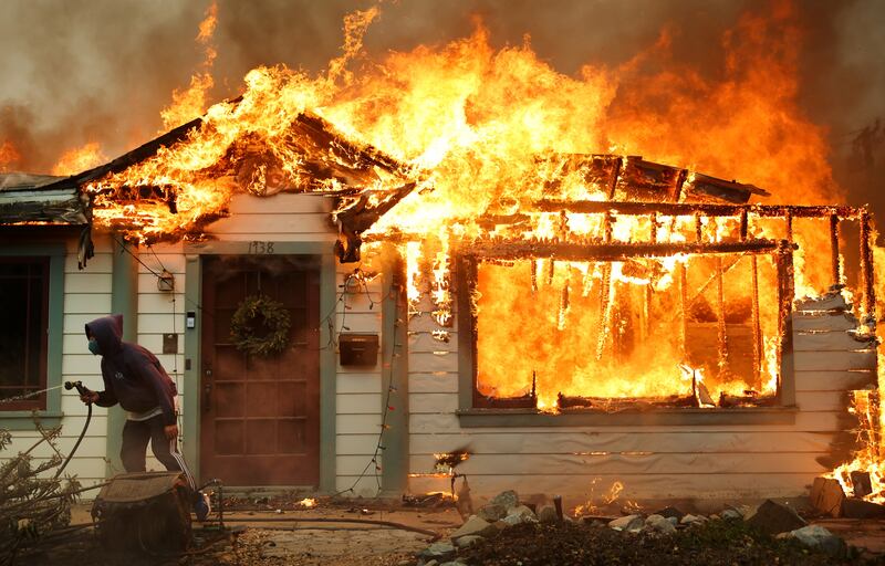 A person attempt's to battle a fire with a garden hose.