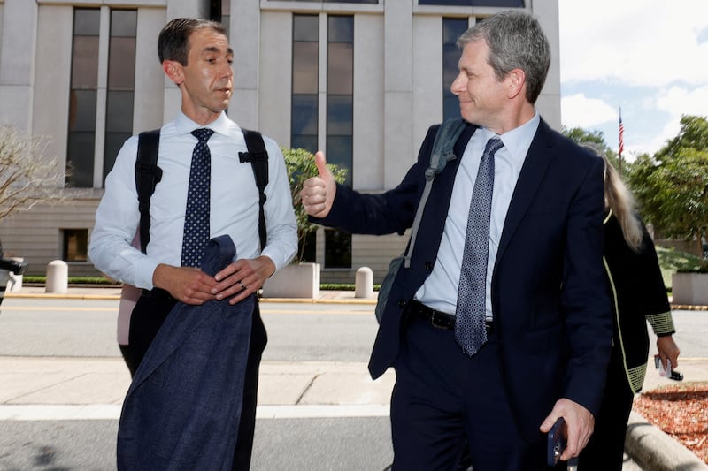 A man in a suit and tie giving a thumbs up to a man in a white shirt and tie outside a large building