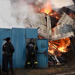 Emergency personnel work to put out a fire before a blue building.
