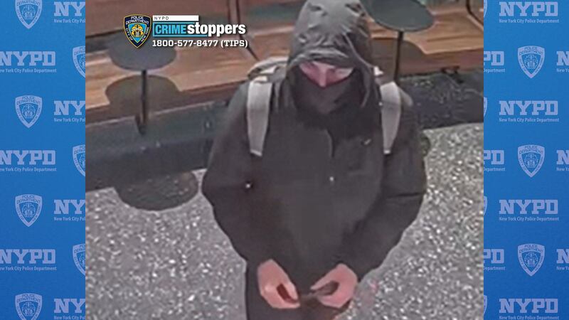A masked man wearing a black jacket stands in a coffee store.