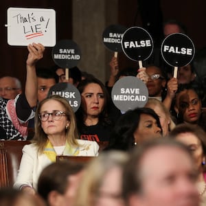 Democrats hold protest signs as Trump speaks.