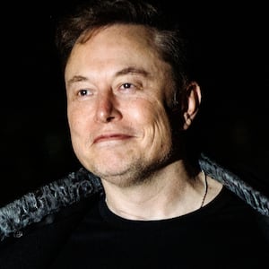 Elon Musk opening his jacket to reveal a t-shirt with the word "DOGE" emblazoned on it.