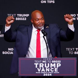 Mark Robinson raises his hands while standing behind a Trump-Vance branded podium.