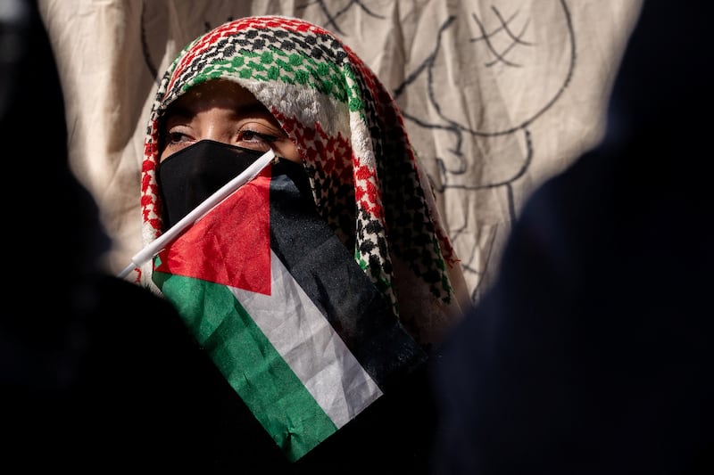 A person stands with a Palestinian flag to protest in support of Palestine.
