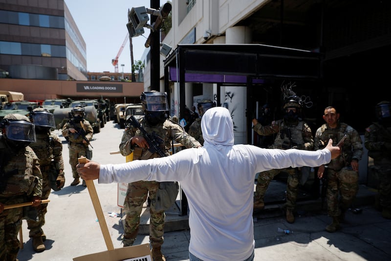 A demonstrator extends their arms during a protest against federal immigration sweeps, as members of the California National Guard stand outside the Edward R. Roybal federal building in Los Angeles.