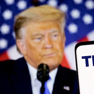 In this picture illustration, the Truth social network logo is seen on a smartphone in front of a display of former U.S. President Donald Trump. 