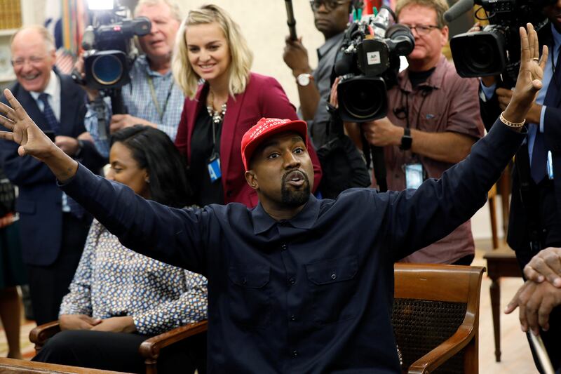 Rapper Kanye West wearing a red MAGA hat waves his hands in the air.
