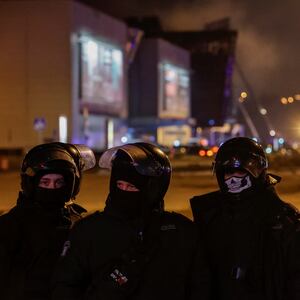 Law enforcement officers in masks stand guard near the burning Crocus City Hall venue