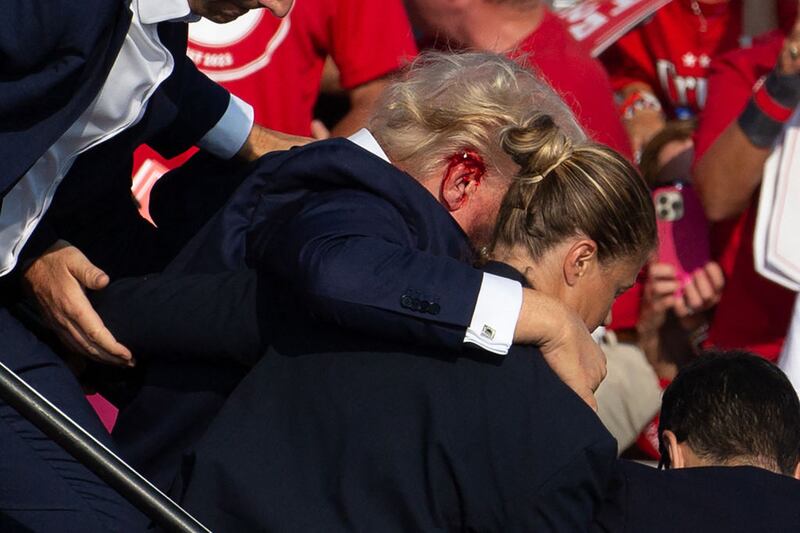 US Republican candidate Donald Trump is seen with blood on his face surrounded by secret service agents as he is taken off the stage at a campaign event at Butler Farm Show Inc. in Butler, Pennsylvania, on July 13, 2024. Trump was hit in the ear in an apparent assassination attempt by a gunman at a campaign rally on Saturday, in a chaotic and shocking incident that will fuel fears of instability ahead of the 2024 US presidential election. The 78-year-old former president was rushed off stage with blood smeared across his face after the shooting in Butler, Pennsylvania, while the gunman and a bystander were killed and two spectators critically injured. (Photo by Rebecca DROKE / AFP) / QUALITY REPEAT (Photo by REBECCA DROKE/AFP via Getty Images)