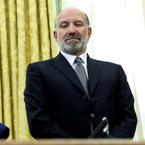 Donald Trump sits at his desk in the Oval Office while Howard Lutnick looks over his shoulder.