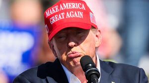 Donald Trump purses his lips while raising his hand on stage at a campaign rally.