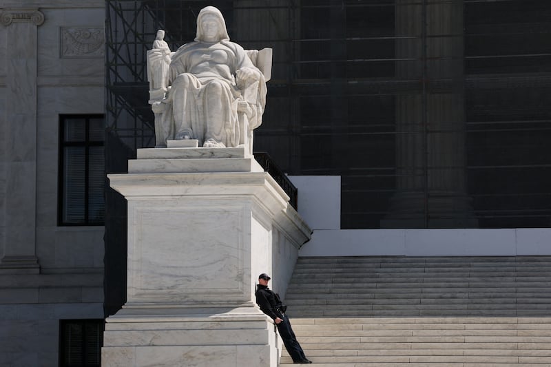 A police officer leans against the "Contemplation of Justice"  statue positioned along the front steps of the U.S. Supreme Court building in Washington, D.C. on April 8, 2025.