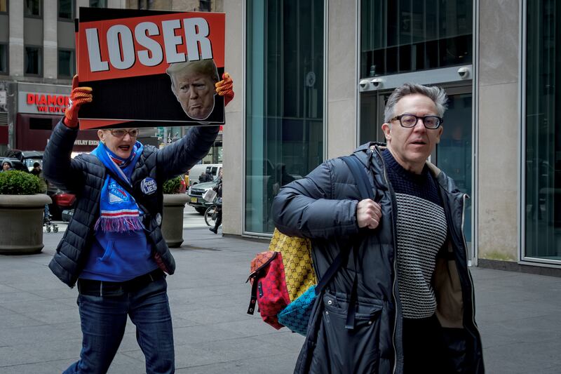 Fox host Greg Gutfeld is followed by a protester holding an anti-Trump sign outside the NewsCorp Building in New York City on January 30, 2024.