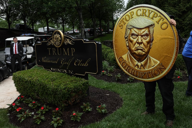 Demonstrators hold up mock crypto currency during the "America is Not for Sale" Rally Against Trump's Crypto Dealings at the Trump National Golf Club on May 22.